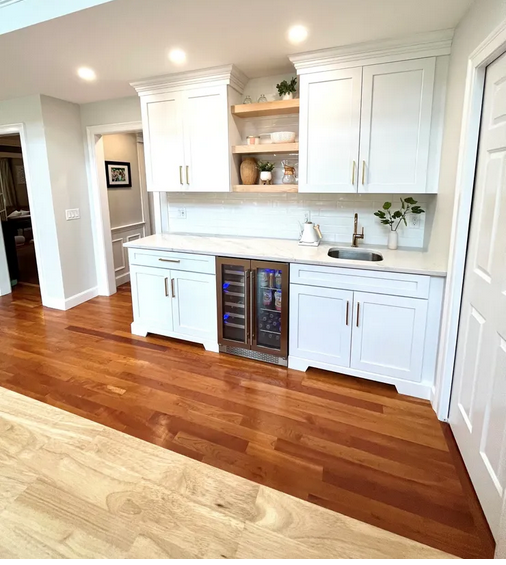 A kitchen with white cabinets and wood floors.