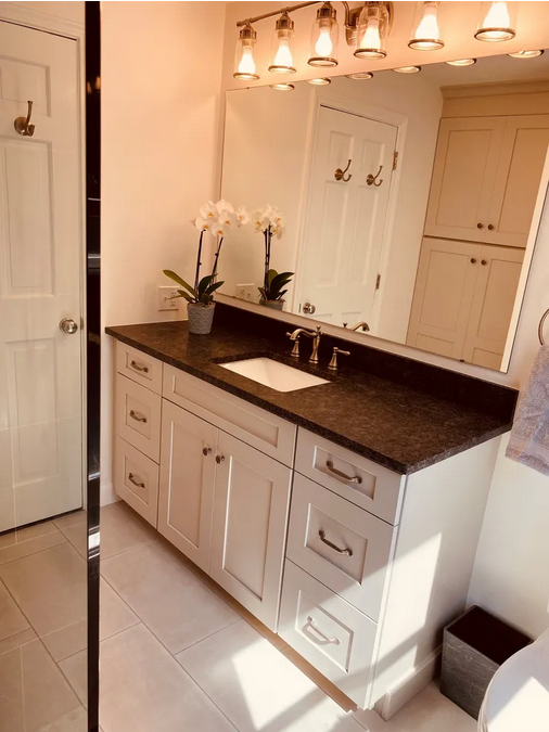 A bathroom with white cabinets and black counter tops.