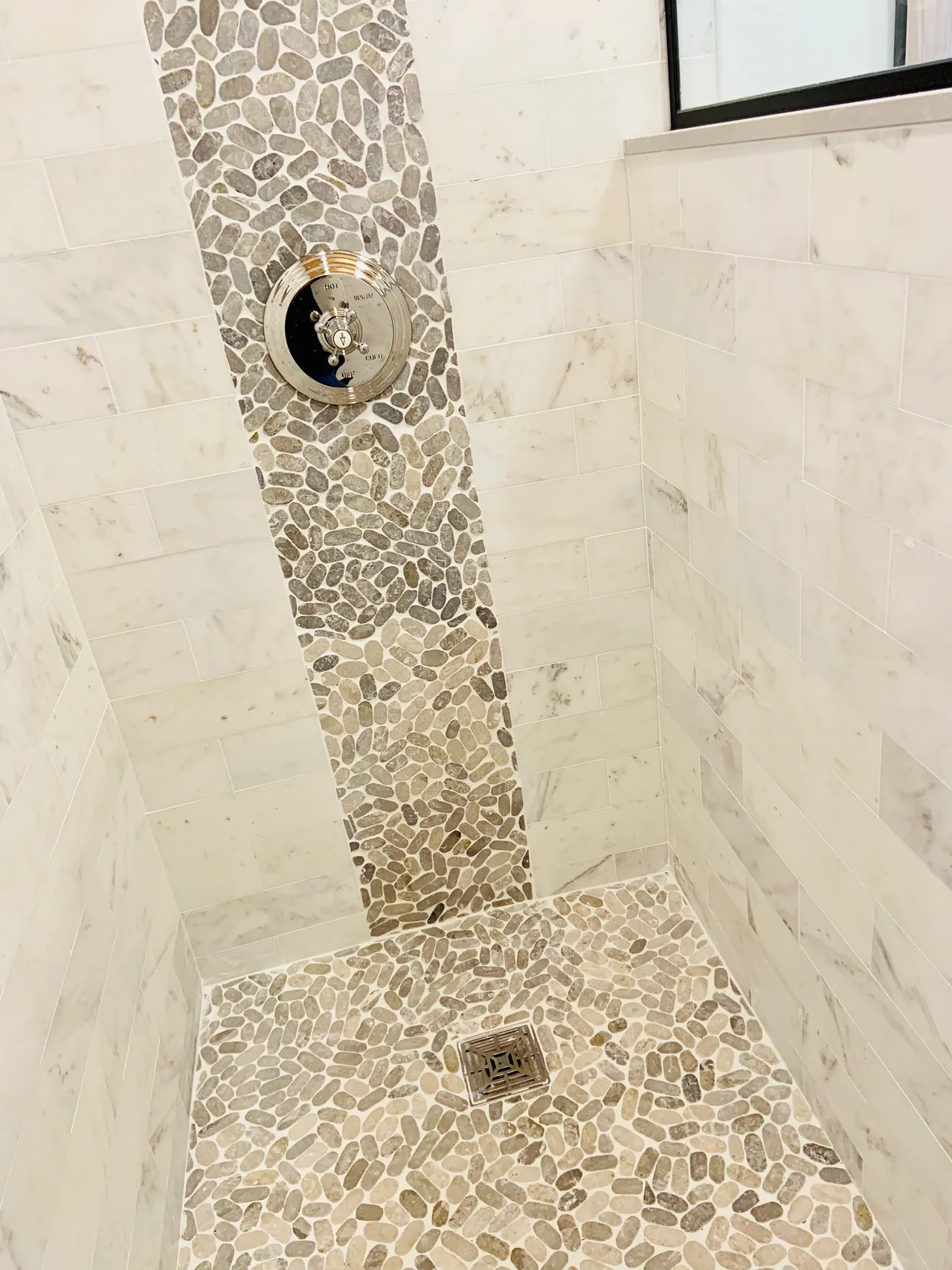 A shower with marble tile and a white wall.