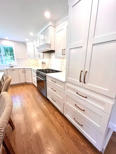 A kitchen with white cabinets and wood floors.