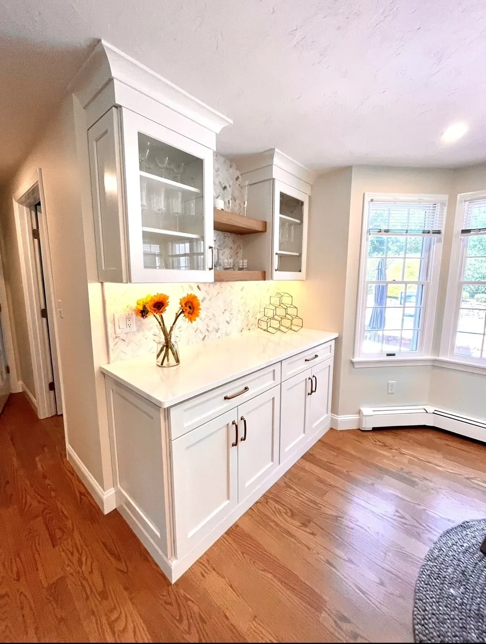 A kitchen with white cabinets and wood floors.