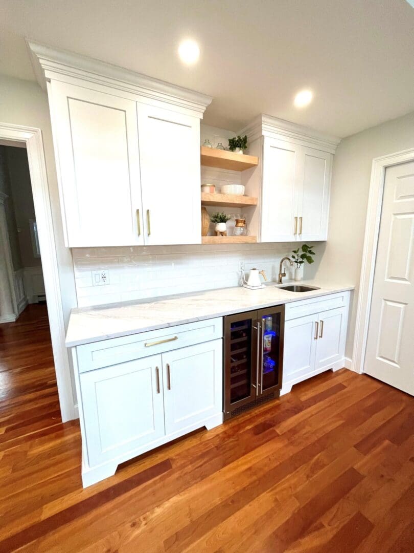 A kitchen with white cabinets and wood floors.