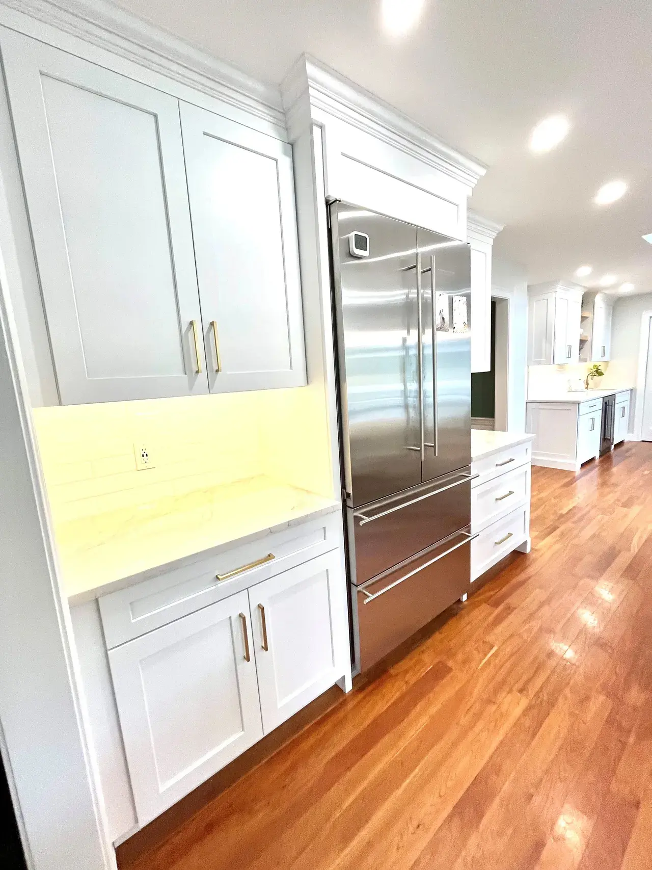 A kitchen with white cabinets and wood floors.