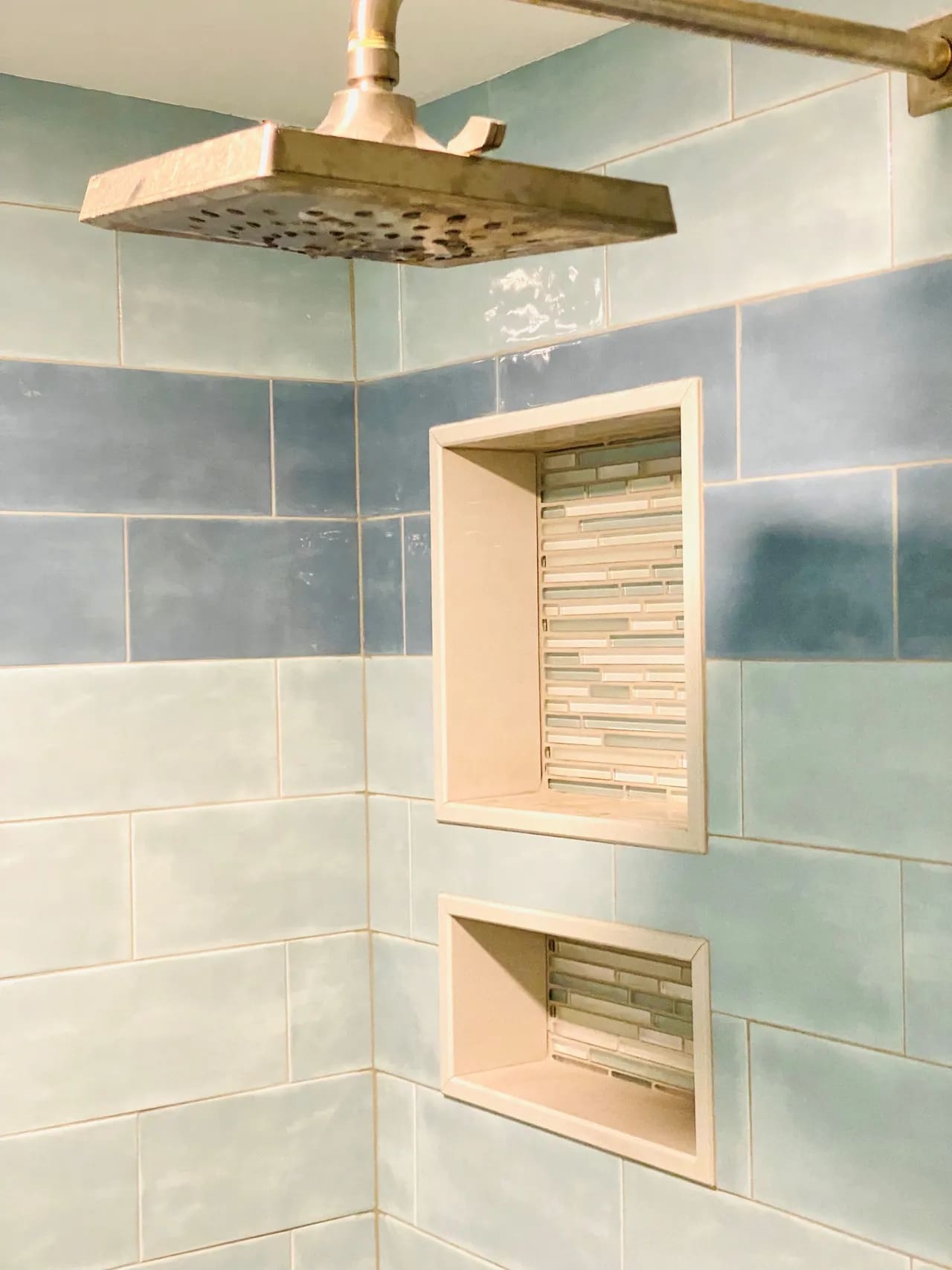 A tiled shower with a wooden shelf and blue tiles.