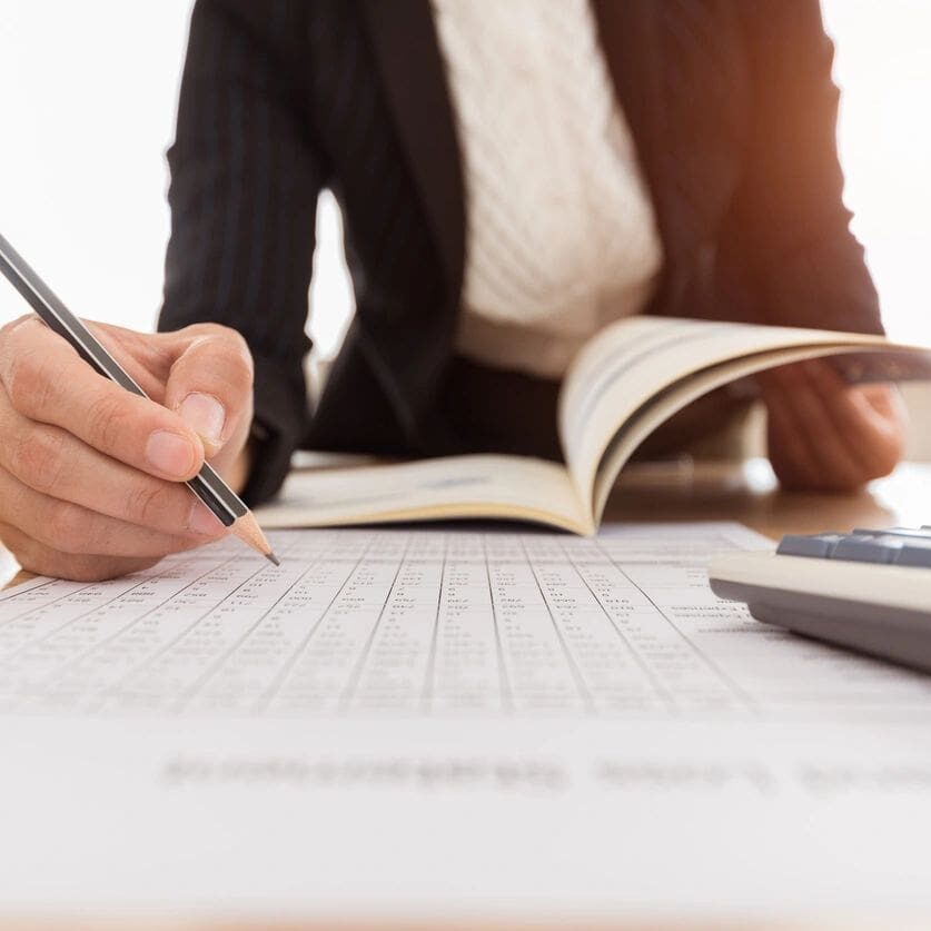 A person writing on paper with a pen and calculator.