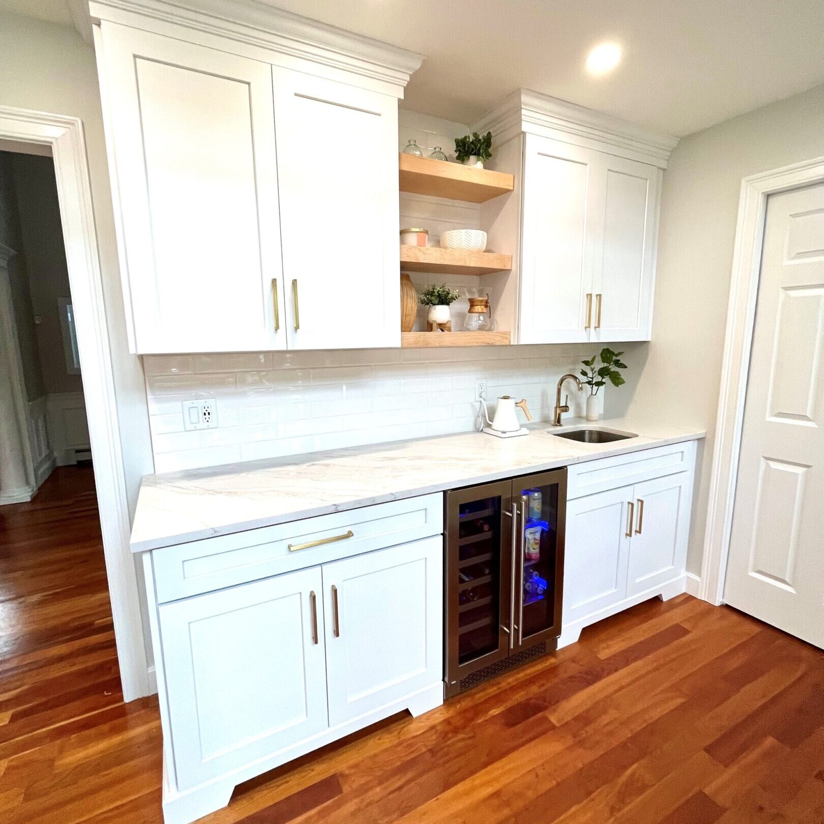 A kitchen with white cabinets and wood floors.